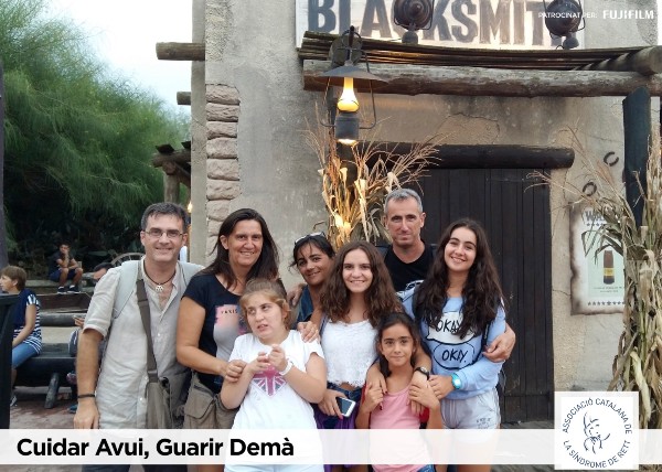  Peu de foto, logo de l'Associació Catalana de la Síndrome de Rett. Fotografia d’una família a  la sortida d’un restaurant envoltant amb carinyo a  una afectada amb la síndrome de rett. 